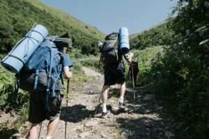 Two backpackers ascending a sunny, rocky mountain path with trekking poles in hand.