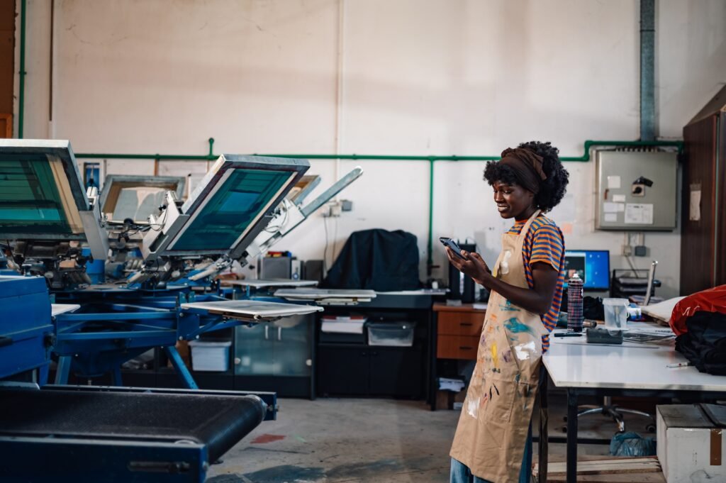 Interracial silkscreen printing shop worker taking orders on cellphone for custom bags