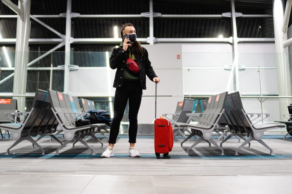young Latino male on a phone call at the airport, standing in the waiting room with his carry-on bag
